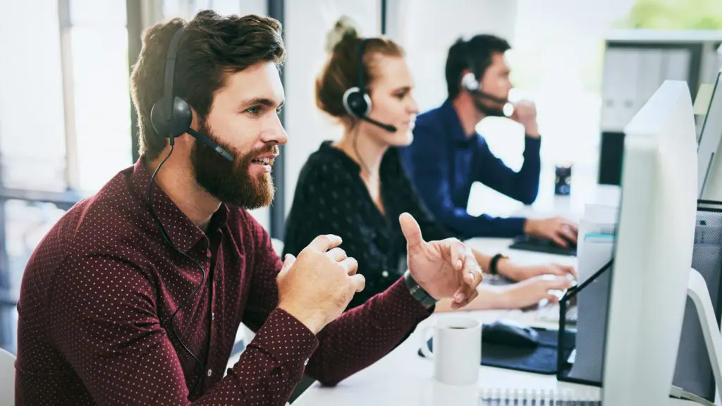 three members of staff working in an office all with headsets on